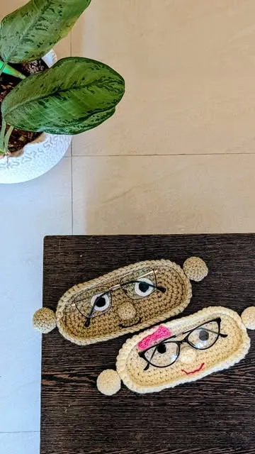 Two crochet spectacle pouches with stitched faces and glasses